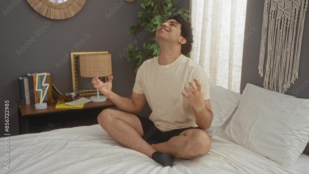 Young hispanic man sitting on bed in pyjama, wearing frustration with mad shouting expression, arms raised crazy yelling in bedroom room Young hispanic man sitting on bed in pyjama, wearing frustration with mad shouting expression, arms raised crazy yelling in bedroom room