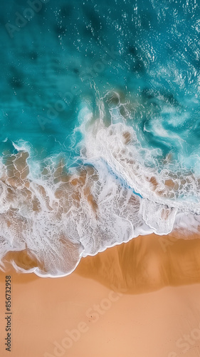 Aerial view of turquoise ocean waves crashing onto a sandy beach, showcasing nature's beauty from above.
