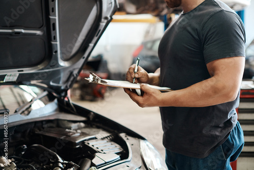 Clipboard, hands and mechanic in garage with car service, maintenance or auto insurance. Checklist, engine and man in workshop for inspection, motor repair and quality assurance at small business.