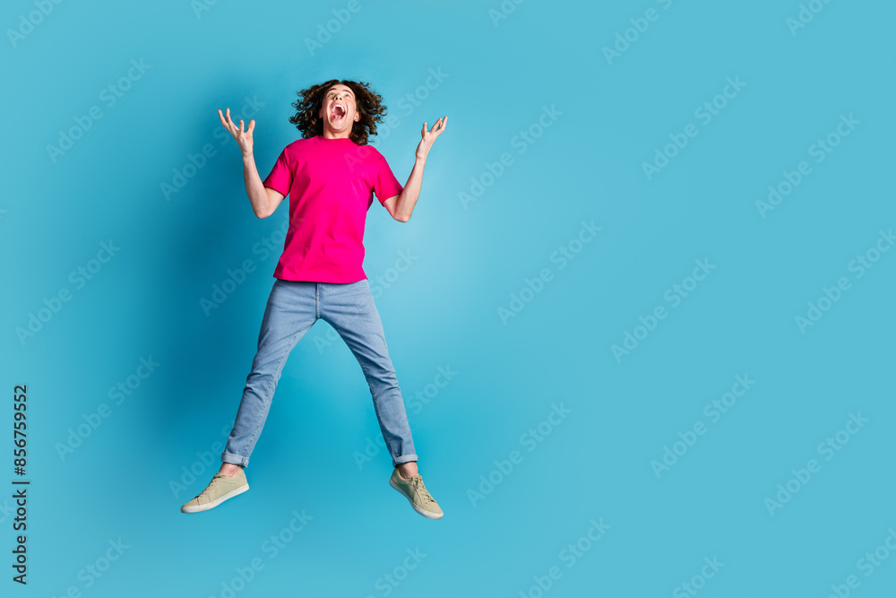 Full size photo of nice young man jump empty space advert wear t-shirt isolated on blue color background Full size photo of nice young man jump empty space advert wear t-shirt isolated on blue color background