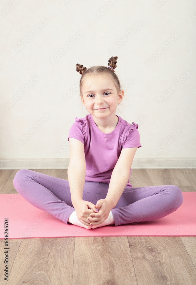 Charming little girl is smiling while doing yoga. Vertical photo Charming little girl is smiling while doing yoga. Vertical photo