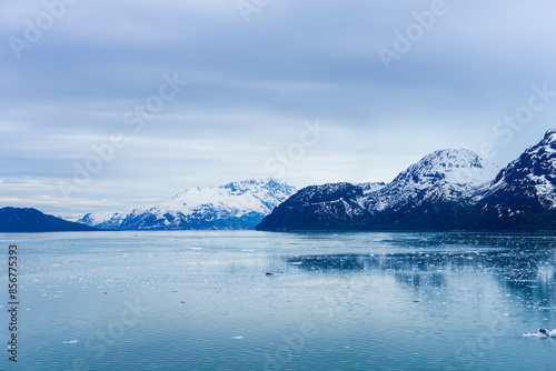 Snow-capped mountains with reflection in the icy waters. Small icebergs floating in the ocean. Alaska.