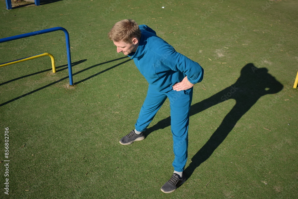 Obraz premium A focused young athlete dynamically performing warm-up drills and stretches outdoors. Clad in athletic gear, he meticulously prepares body for the physical demands ahead through a regimented routine