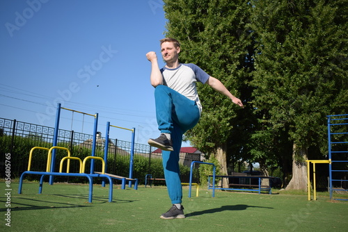 A focused young athlete dynamically performing warm-up drills and stretches outdoors. Clad in athletic gear, he meticulously prepares body for the physical demands ahead through a regimented routine
