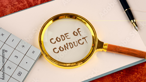 Business and code of conduct concept. Copy space. Code of conduct symbol written in the business book of the head with a magnifying glass on top near the calculator and a pen in the composition photo