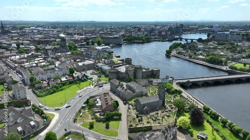 King John's Castle, Limerick, Ireland, May 2024. Drone orbits the historic Medieval Castle passing St Munchin's church and Jones Mausoleum towards the River Shannon on a warm summer day. photo