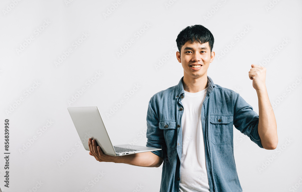 Portrait smiling Asian young man hold a laptop computer studio shot isolated white background, happiness and excited man holding laptop and raising his arm up to celebrate success Portrait smiling Asian young man hold a laptop computer studio shot isolated white background, happiness and excited man holding laptop and raising his arm up to celebrate success
