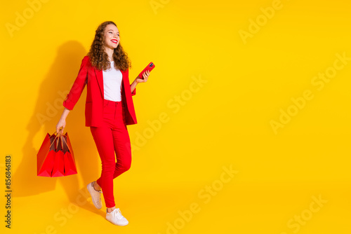 Full body portrait of gorgeous young lady phone bags walk empty space wear red suit isolated on yellow color background