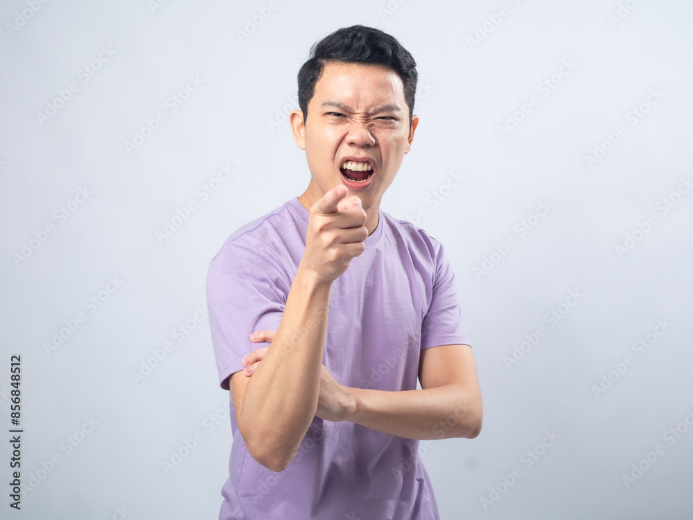 Young Asian man in lavender t-shirt pointing directly at the camera with an intense, angry expression. Studio shot on plain background capturing his casual outfit and expressive Young Asian man in lavender t-shirt pointing directly at the camera with an intense, angry expression. Studio shot on plain background capturing his casual outfit and expressive