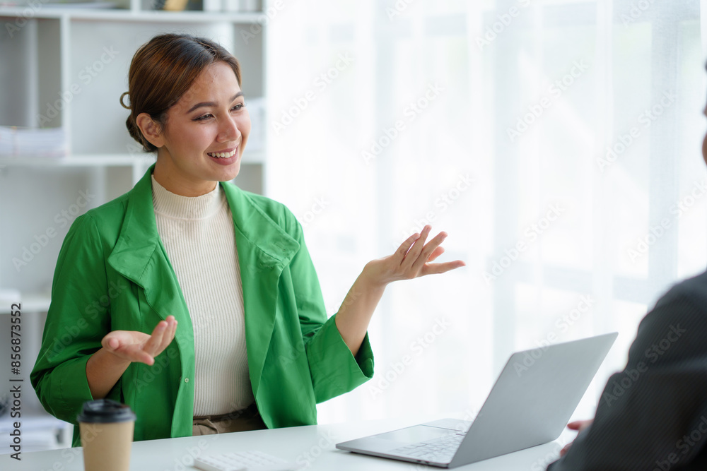 Two asian business partners collaborate in a vibrant office, discussing ideas with laptops open. Smiling and gesturing, they plan and achieve goals in a modern, bright workspace Two asian business partners collaborate in a vibrant office, discussing ideas with laptops open. Smiling and gesturing, they plan and achieve goals in a modern, bright workspace