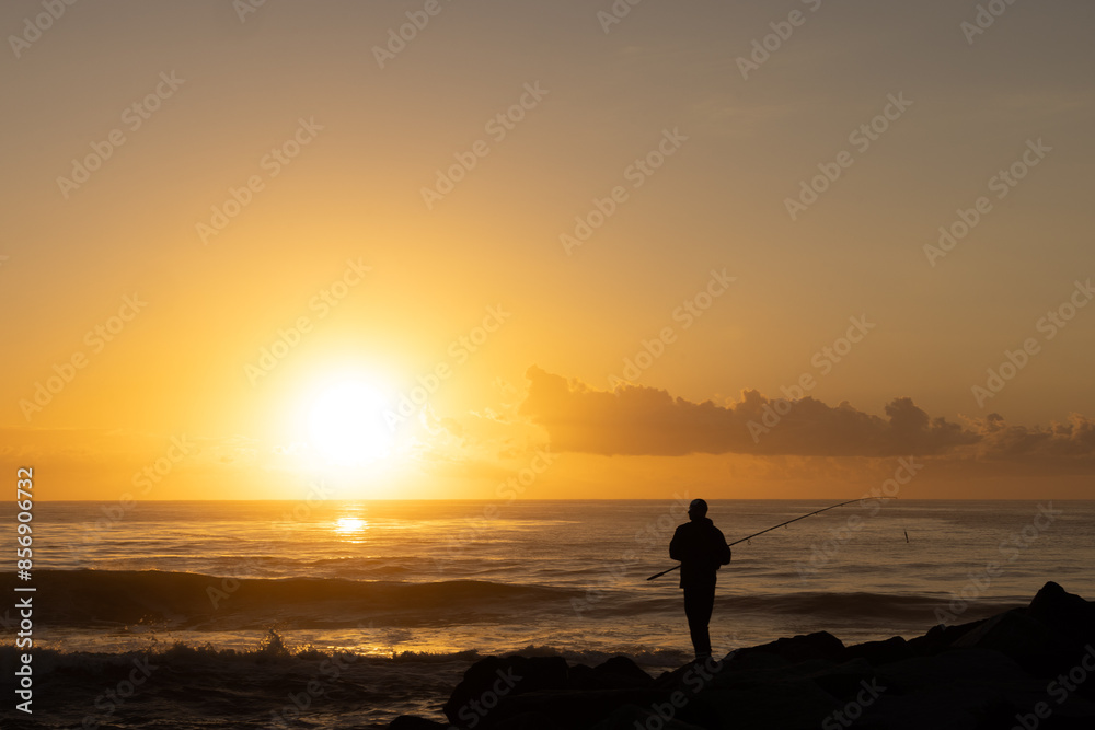Silhouette of man fishing off rocks at sunrise Silhouette of man fishing off rocks at sunrise