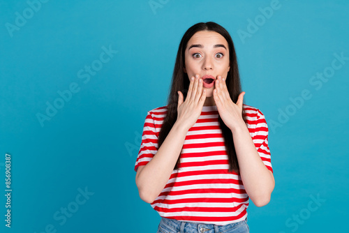 Photo of charming impressed girl wear striped t-shirt arms cheeks empty space isolated blue color background