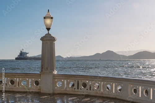 City of Santos, Brazil. Traditional wall and old light pole on the beach. Cargo ship passing on the horizon and silhouette of mountains in the background.