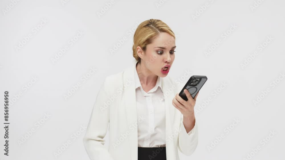 Angry irritated business young woman talking emotionally on a cell phone. A business blonde director scolds her subordinate on the phone on a white background. Angry irritated business young woman talking emotionally on a cell phone. A business blonde director scolds her subordinate on the phone on a white background.
