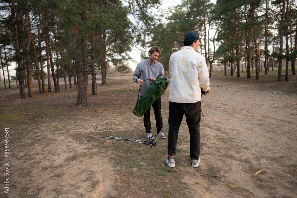 Two men camping in a forest clearing at sunset, preparing their gear for an evening outdoors