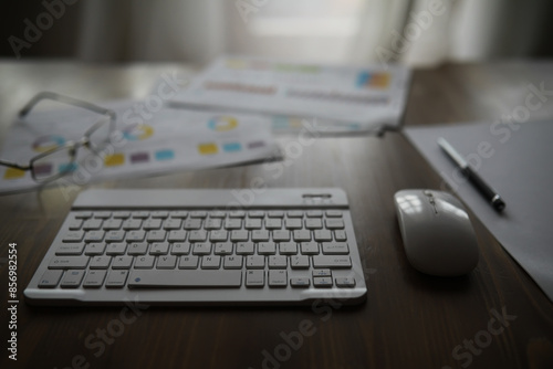 Workplace Setup with Wireless Keyboard, Mouse, and Financial Documents on Wooden Desk