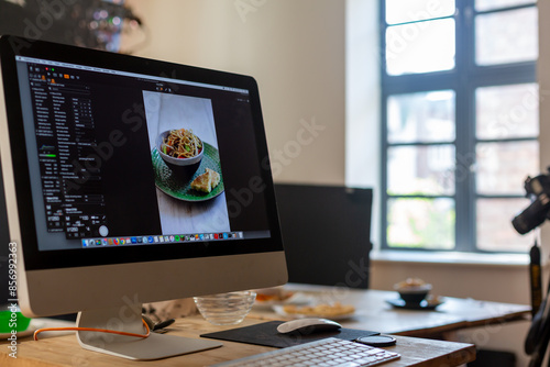 Food photography production set showing computer, keyboard, camera and tripod. Bowl of noodles.