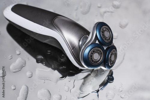 фотографія Close-up of a modern electric shaver lying on a reflective surface with water dr