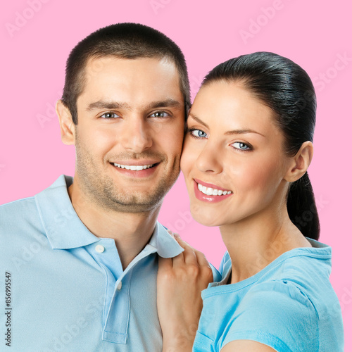 Happy amazed smiling couple. Portrait of standing close embracing models in love studio concept, isolated over rose pink background. Young brunette man and woman posing together. Copy space for text.