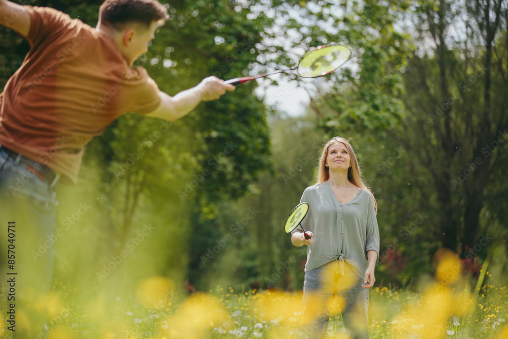 A young man and his girlfriend spend time together playing badminton on a lawn in a park. A young man and his girlfriend spend time together playing badminton on a lawn in a park.