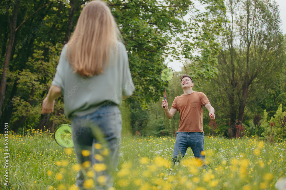 A young man and his girlfriend spend time together playing badminton on a lawn in a park. A young man and his girlfriend spend time together playing badminton on a lawn in a park.