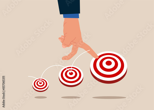 Human hand  jumping on bigger and higher archery bull's eye target. Aspiration and motivation to achieve bigger business target, advancement in career or business growth concept.