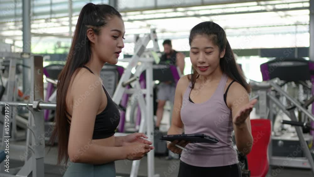 Personal trainer and client discussing fitness goals and workout plans in a modern gym setting. Engaging consultation with tablet technology