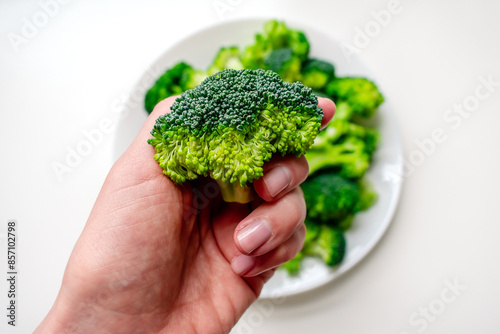 Broccoli in a woman's hand against the background of a plate of broccoli. Broccoli on a white plate.