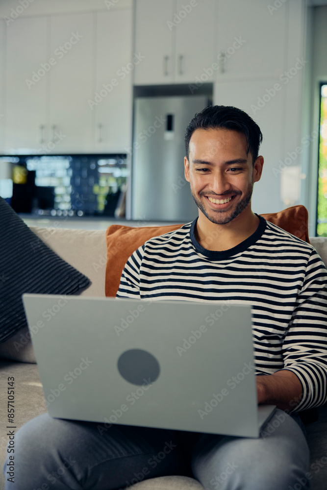 A man is smiling, using a laptop on the couch for comfort and happiness A man is smiling, using a laptop on the couch for comfort and happiness