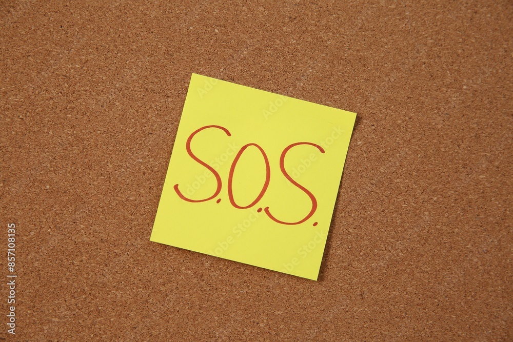 Note with word SOS and stationery on cork board, closeup Note with word SOS and stationery on cork board, closeup