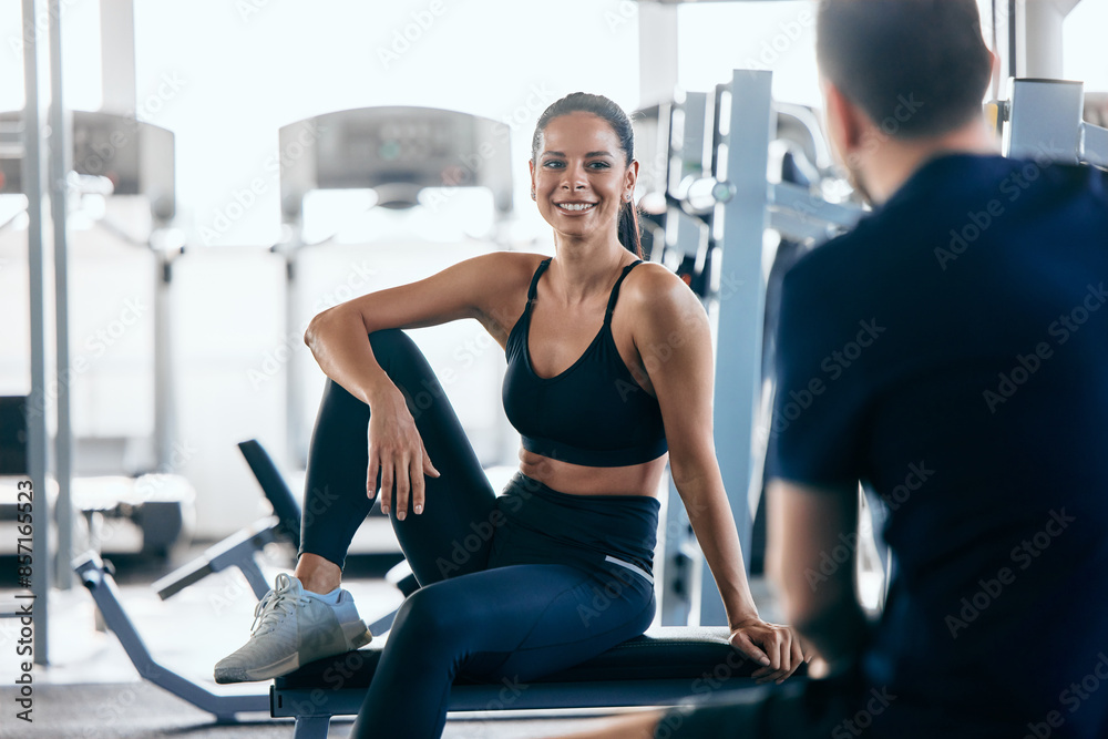 A smiling girl sitting on a bench and talking to her gym partner, resting together. A smiling girl sitting on a bench and talking to her gym partner, resting together.