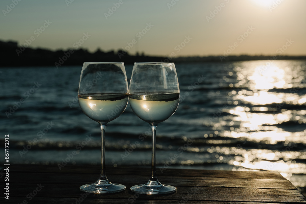 Two glasses of wine on wooden table near river at sunset. Space for text Two glasses of wine on wooden table near river at sunset. Space for text