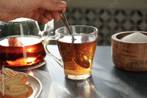 Woman stirring tea with spoon at dark table, closeup