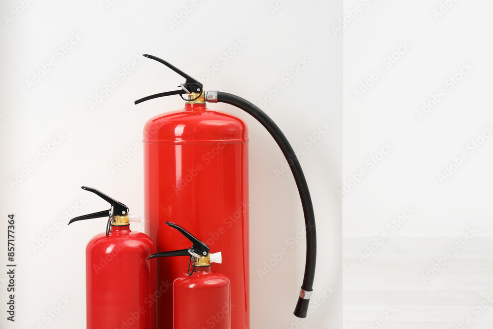 Fire extinguishers near light wall indoors, space for text