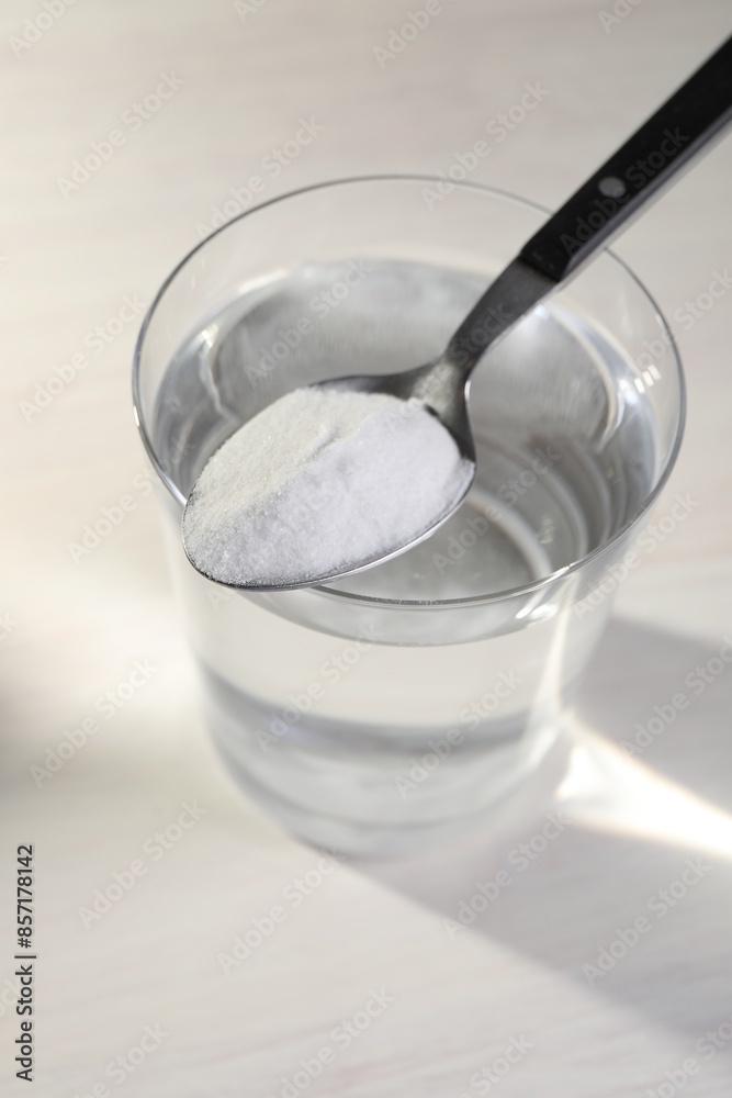 Glass of water and spoon with baking soda on light background Glass of water and spoon with baking soda on light background