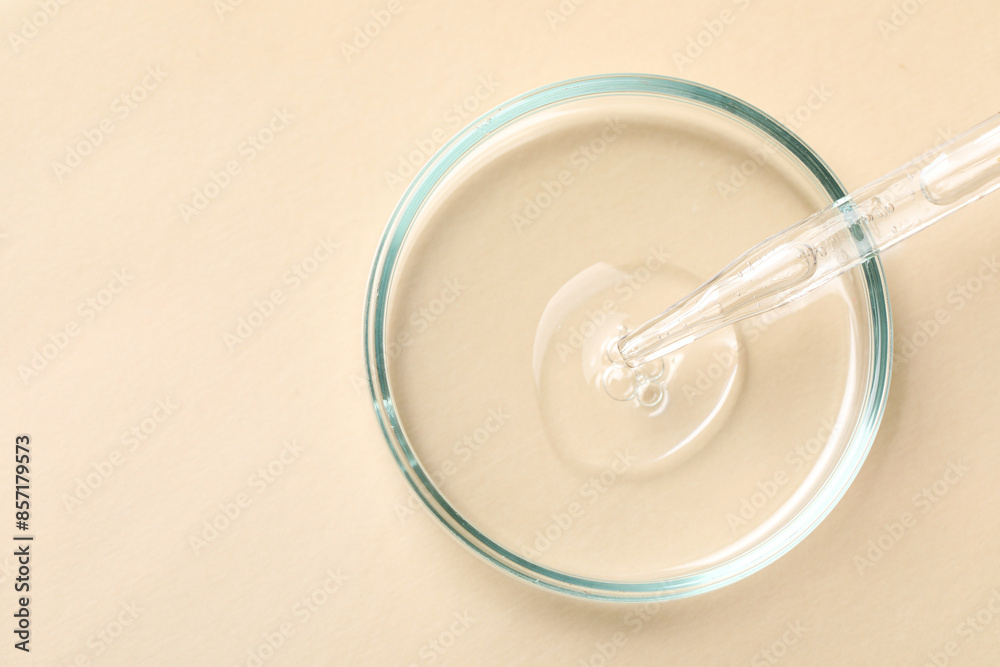 Glass pipette and petri dish with liquid on beige background, top view. Space for text Glass pipette and petri dish with liquid on beige background, top view. Space for text