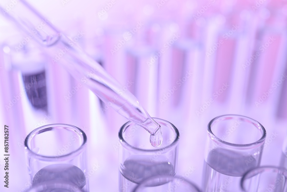 Dripping liquid from pipette into test tube on violet background, closeup Dripping liquid from pipette into test tube on violet background, closeup