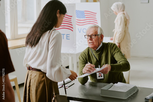 фотографія Senior Caucasian electoral district worker sitting at desk at polling station ex