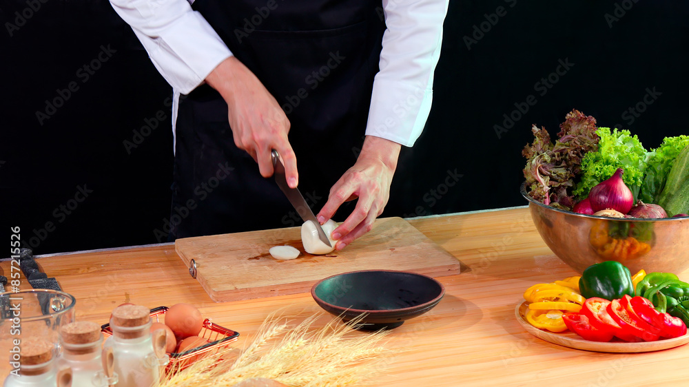 Young Chef slicing white onion on cutting board with fresh vegetables, eggs, and spices on kitchen counter Young Chef slicing white onion on cutting board with fresh vegetables, eggs, and spices on kitchen counter