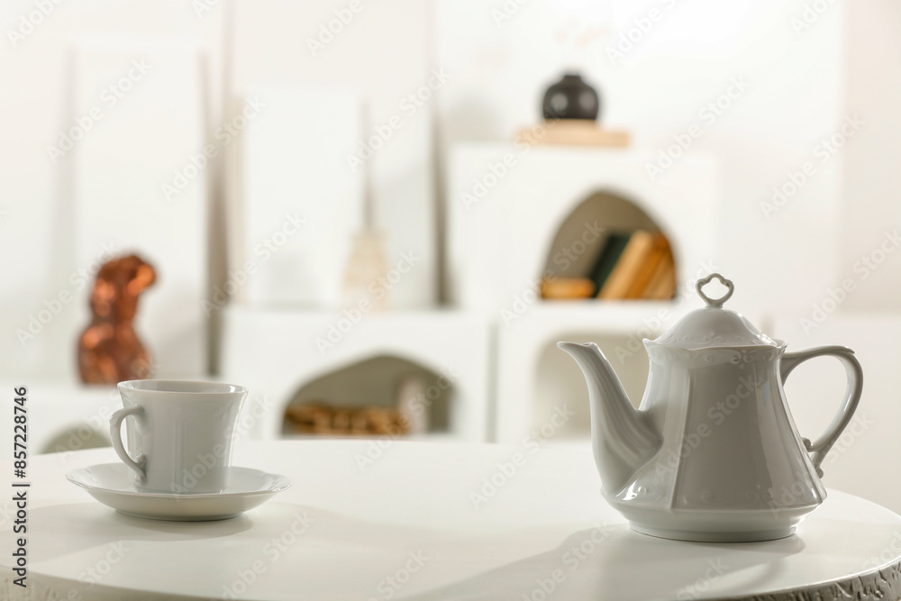 Set of different dishes and cups and saucers and coffee pot on white table top with blurred white kitchen interior