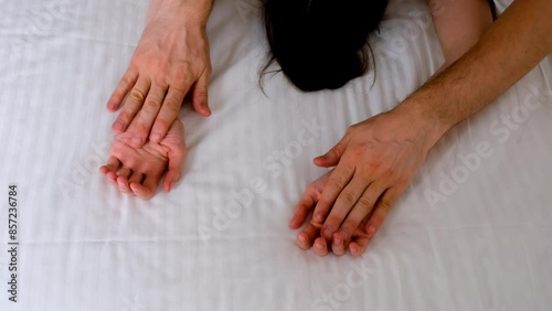Man is stroking woman's hands lying in bed with white linen making love, hands close-up. Sex, intimate life, pleasure and love concept. Two lovers having a sex holding hands, sensual gesture.