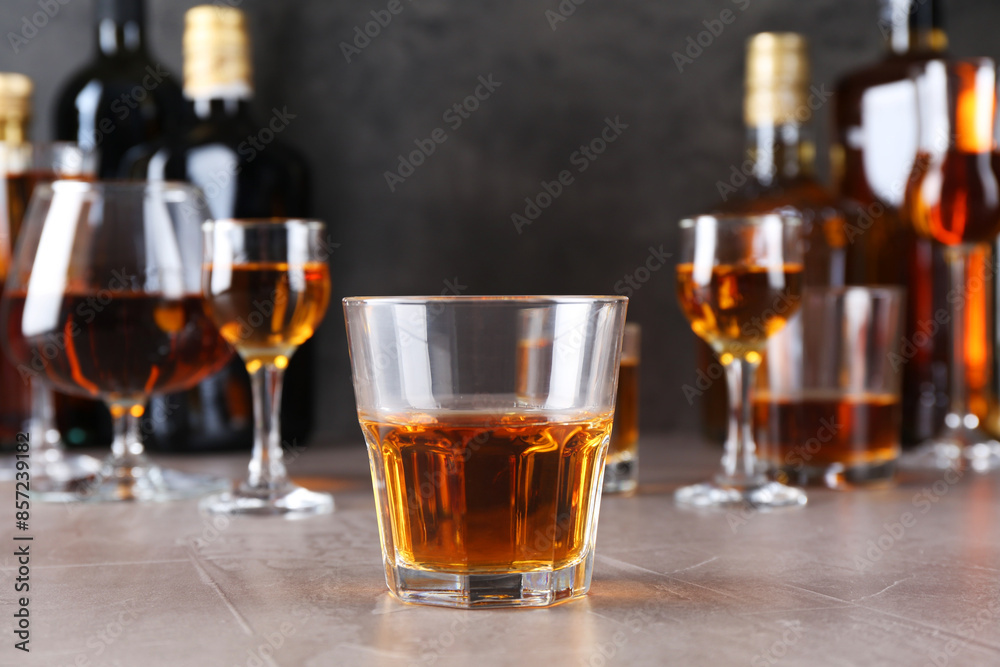 One liqueur in glass in front of others on grey textured table, closeup One liqueur in glass in front of others on grey textured table, closeup