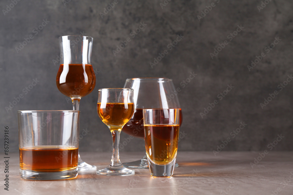 Many different liqueurs in glasses on grey textured table. Space for text Many different liqueurs in glasses on grey textured table. Space for text