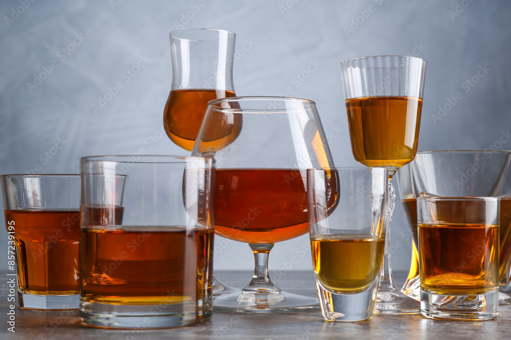 Different liqueurs in glasses on grey table, closeup Different liqueurs in glasses on grey table, closeup