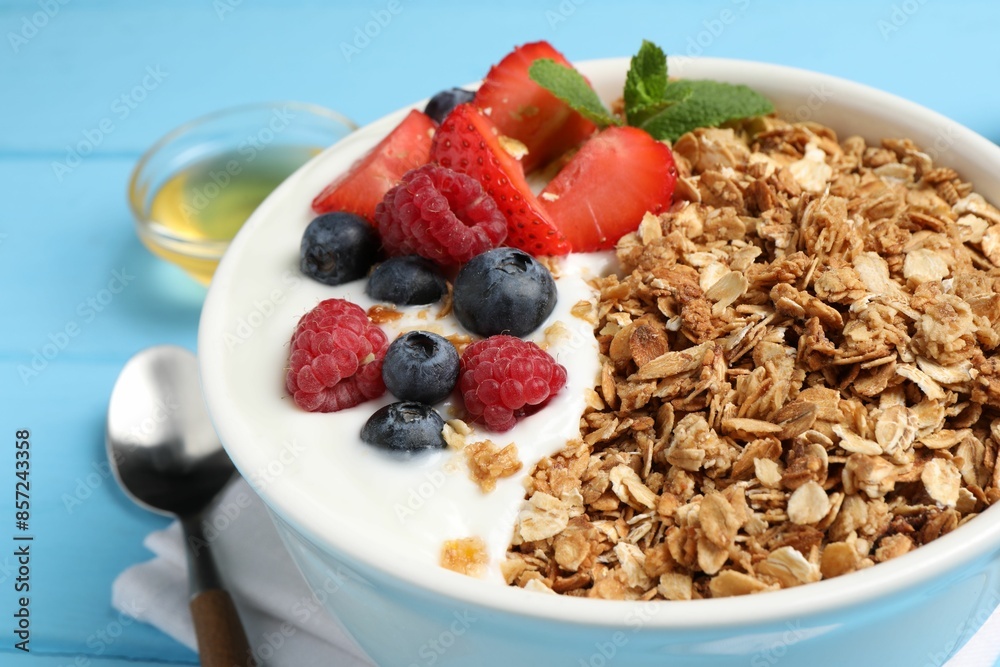 Tasty granola with berries and yogurt in bowl on light blue table, closeup Tasty granola with berries and yogurt in bowl on light blue table, closeup