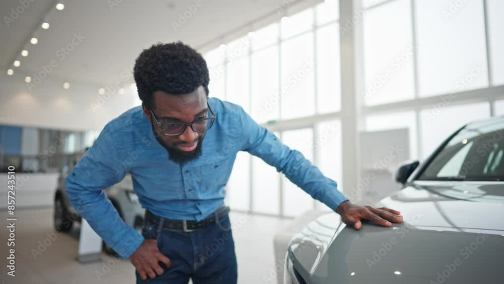 Handsome African American man observing luxury car with focus. Happy customer enjoying time while choosing automobile in auto salon. Smiling with joy while looking at camera. Buying concept. Handsome African American man observing luxury car with focus. Happy customer enjoying time while choosing automobile in auto salon. Smiling with joy while looking at camera. Buying concept.