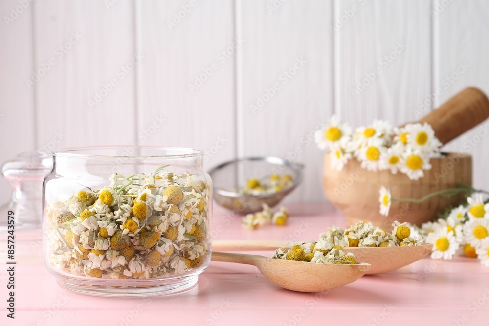 Chamomile flowers in glass jar and spoons on pink wooden table Chamomile flowers in glass jar and spoons on pink wooden table
