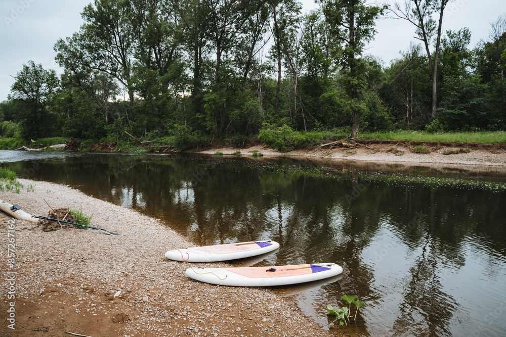 Two white SUP boards are parked on the river bank, sports camping equipment, supdording on a mountain river. Two white SUP boards are parked on the river bank, sports camping equipment, supdording on a mountain river.