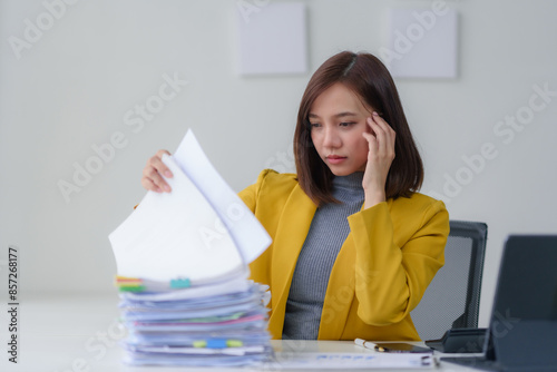 Frustrated woman dealing with paperwork at her desk, feeling stressed and overwhelmed at the office, representing a busy workday.