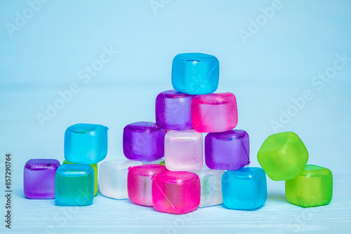 Pile of colorful reusable plastic ice cubes with various colors including pink, purple, green, blue and white on a light blue wooden surface.